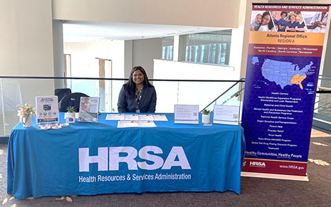 A staff member seated at a HRSA information booth at the WHIAANHPI conference. 