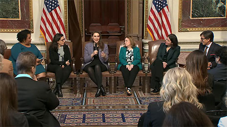 Attendees seated in a row of chairs at the White House Cervical Cancer Forum engage in a panel discussion. Jane Segebrecht holds a microphone while speaking.