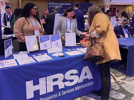 HRSA staff table an exhibition event as a participant leans in for information