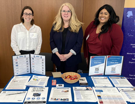 HRSA Administrator Carole Johnson and two HRSA staff members pose in front of a HRSA  event table