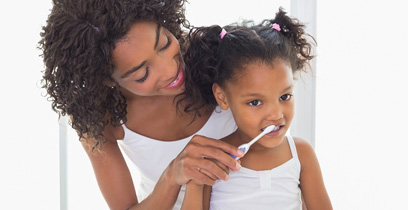 Mother helping young daughter brush her teeth.