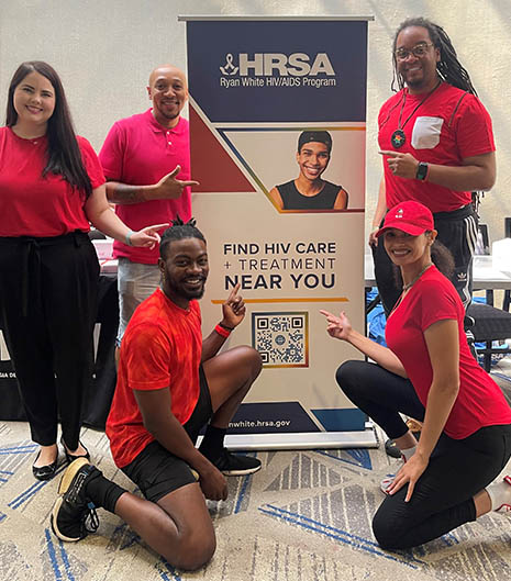 Group portrait of members of the HRSA HIV/AIDS Bureau at Atlanta Black Pride Event booth.
