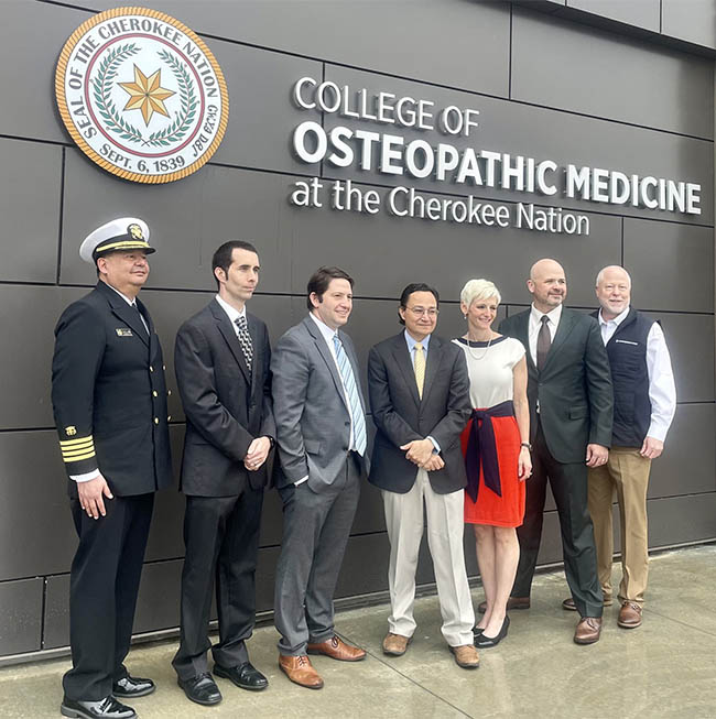 HRSA Deputy Administrator Jordan Grossman and HRSA Tribal Advisory Council members stand together for portrait in front of the College of Osteopathic Medicine at the Cherokee Nation. 
