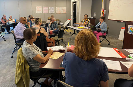 Attendees at the HRSA Region 9 grant writing workshop sit at tables in a meeting room while listening to the presenter at the front of the room.