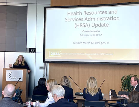 HRSA Administrator Carole Johnson presents from a podium. The screen reads, Health Resources and Services Administration (HRSA) Update