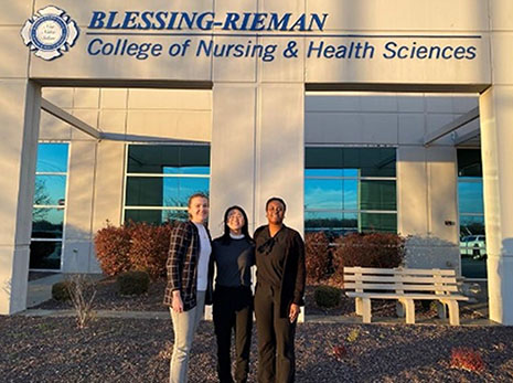 Three individuals pose for a photo outside of the Blessing-Rieman College of Nursing & Health Sciences.