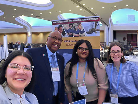 Four members of HRSA staff pose for a photograph in front of the HRSA exhibition