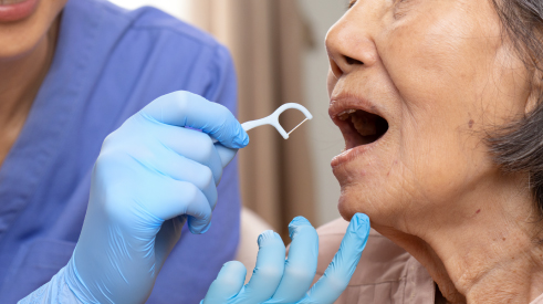 A health care professional using a floss holder to floss an older woman’s teeth.