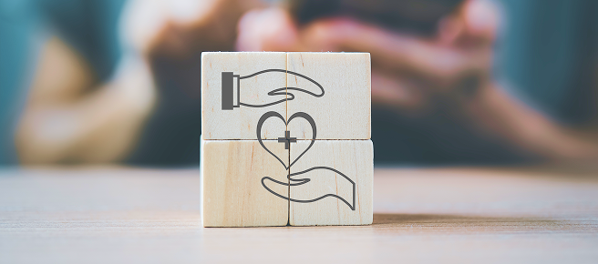 Four blocks are placed together to make a square. The square depicts two hands holding a heart.