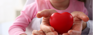 A person is holding a fake heart in their hands, while a child is sitting with them.