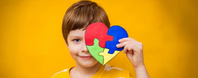  A young boy in a stripped shirt holding a puzzle heart in front of his face. 
