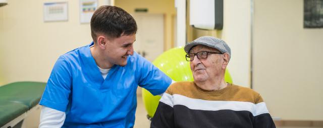 A male nurse sits with an older adult patient. 