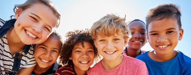 A close up image of group of pre-teen children smiling in a park. 