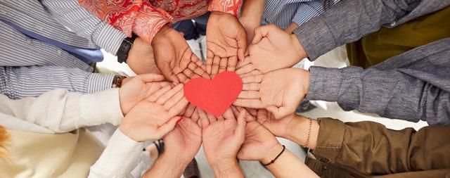 Group of people with outstretched hands holding  a red paper heart symbol. 