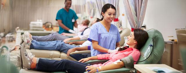  A woman smiling while donating blood while a healthcare worker smiles back at her. 