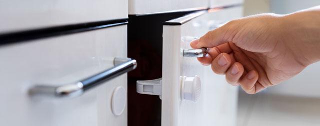 A hand closing a cabinet that contains a child lock. 